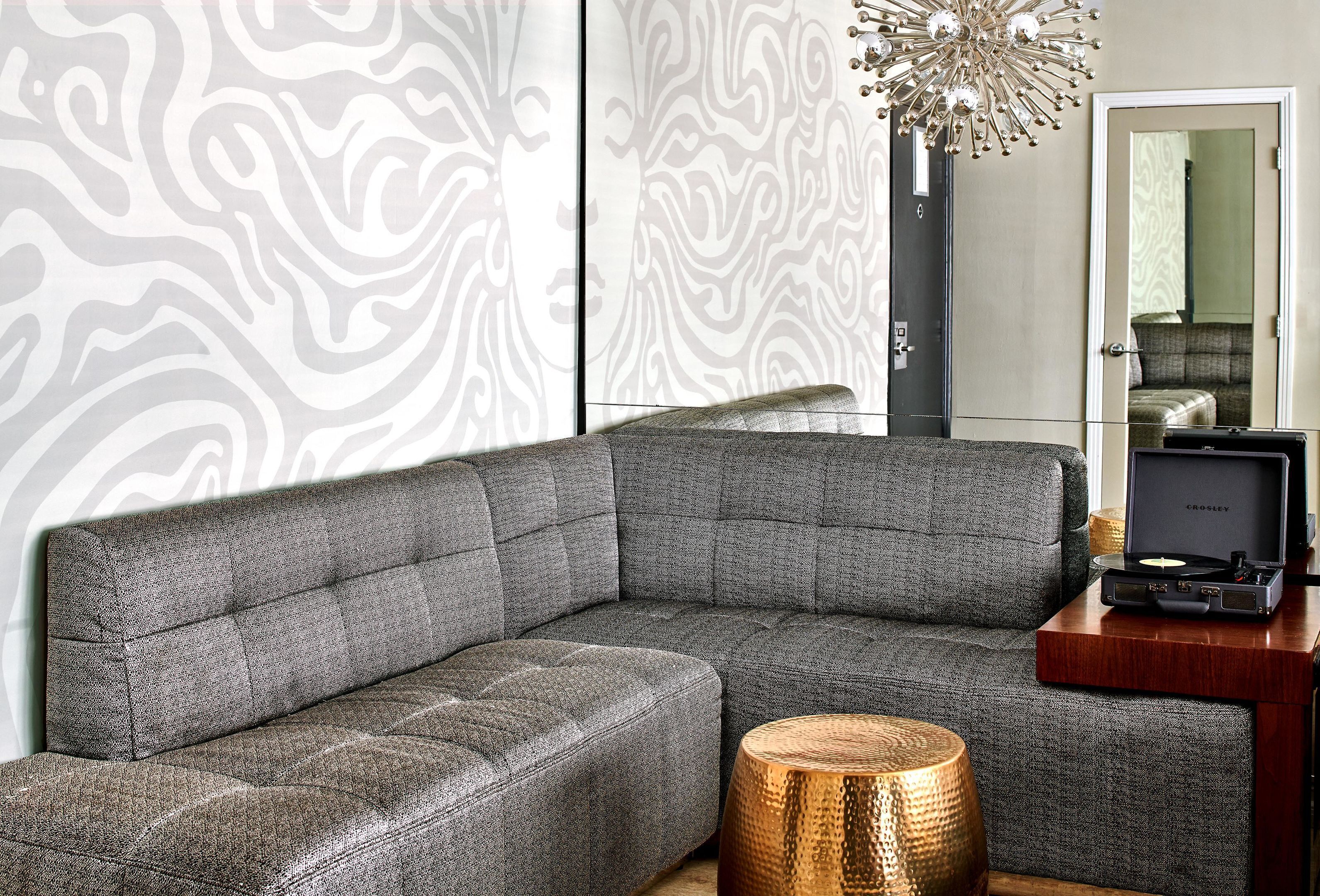 A sectional sofa with a built-in speaker system, a round wooden side table, and a patterned wall.