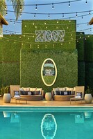 A poolside area with a green wall, a sign reading "FREE THE MUSIC," and a lounge with wicker furniture and pillows.