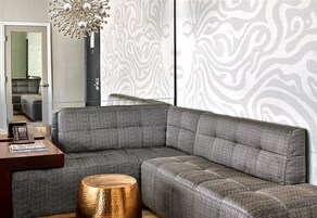 A modern living room with a sectional sofa, a wooden coffee table, a decorative floor lamp, and a patterned wall.