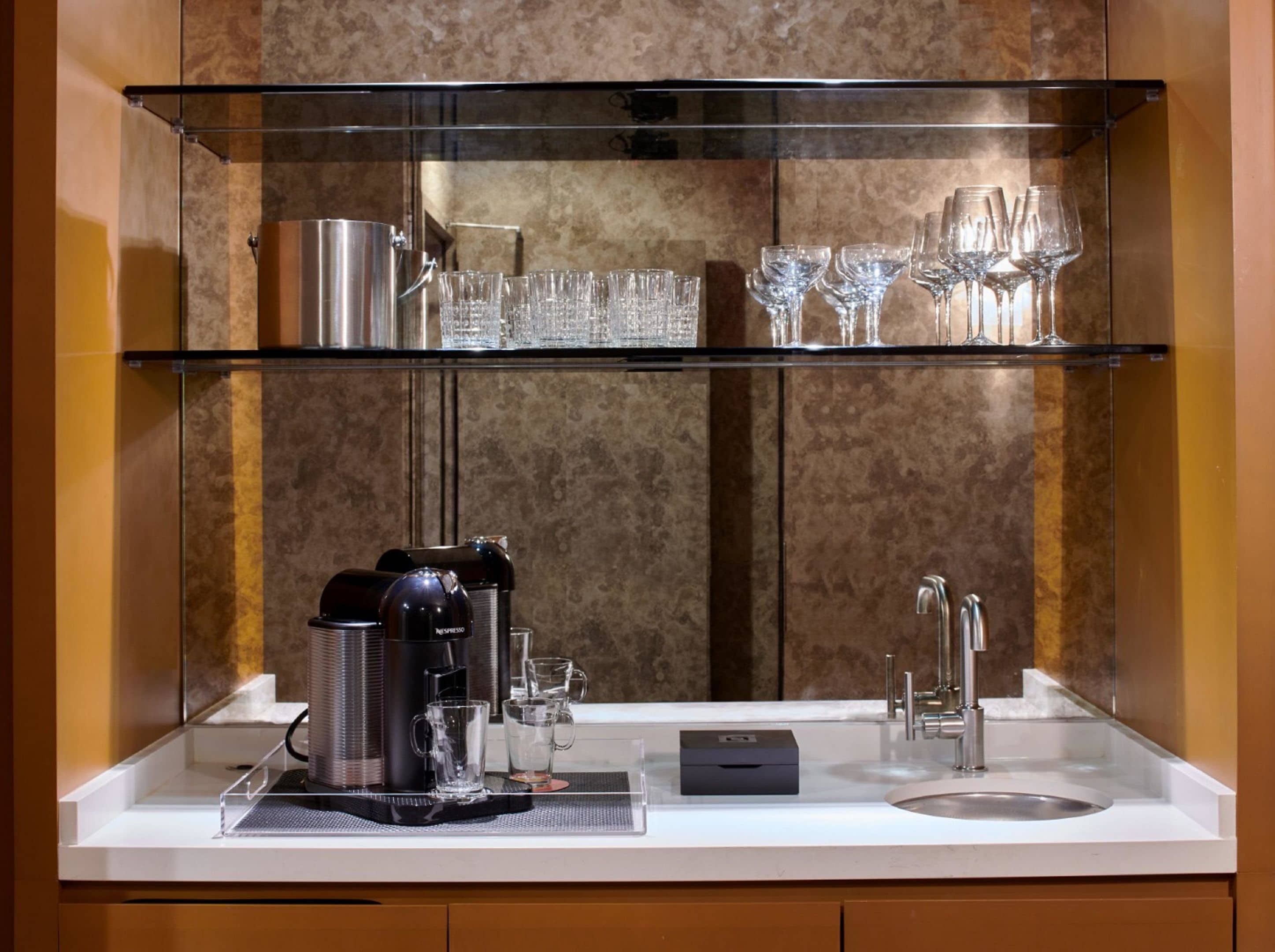 Una barra equipada con una cafetera, vasos y un lavabo.