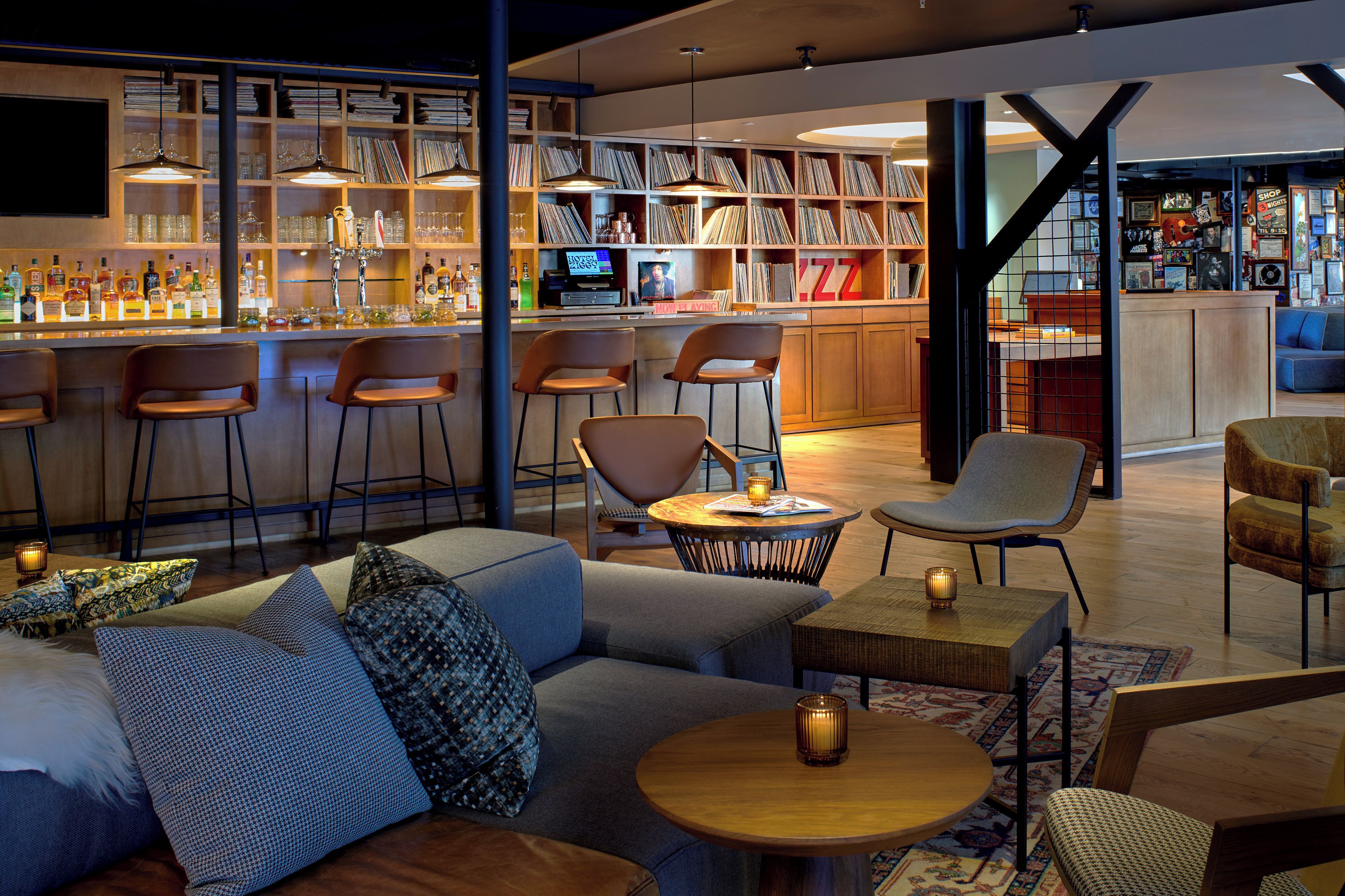 A bar area with shelves of bottles, a counter, and bar stools. There is a seating area with sofas and a round table.