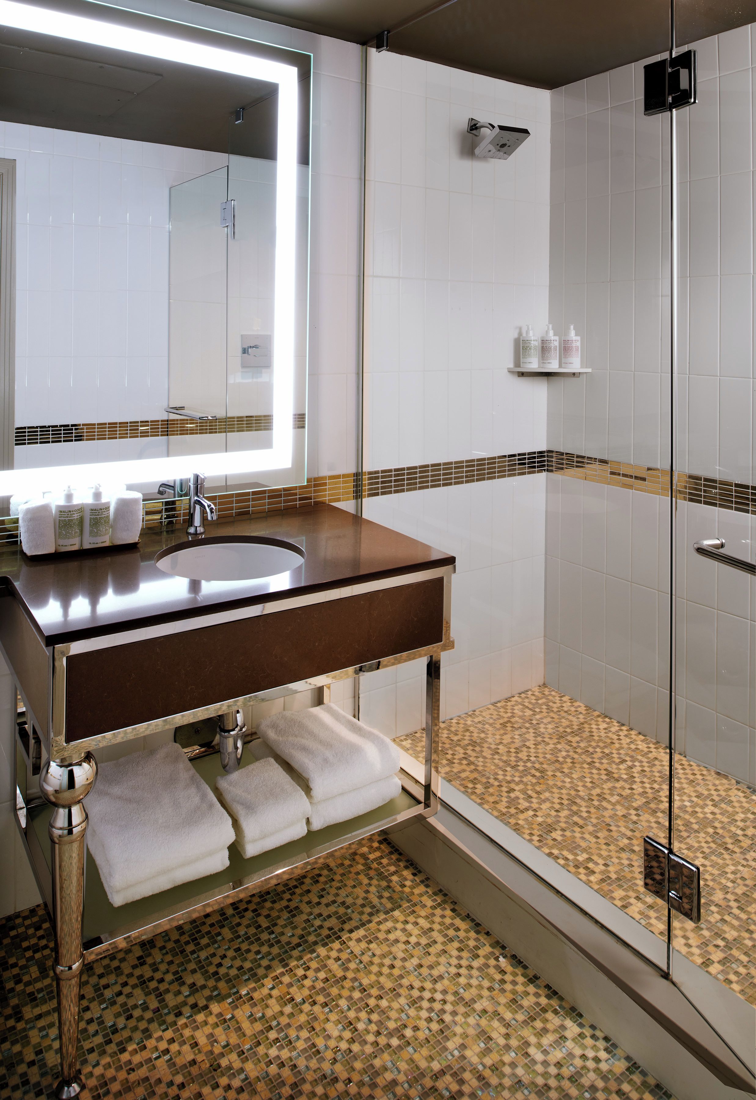 A modern bathroom with a glass shower enclosure, a vanity with a mirror, and a tiled floor.
