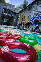 Un área de piscina con varios flotadores inflables de colores y un edificio con un mural distintivo al fondo.