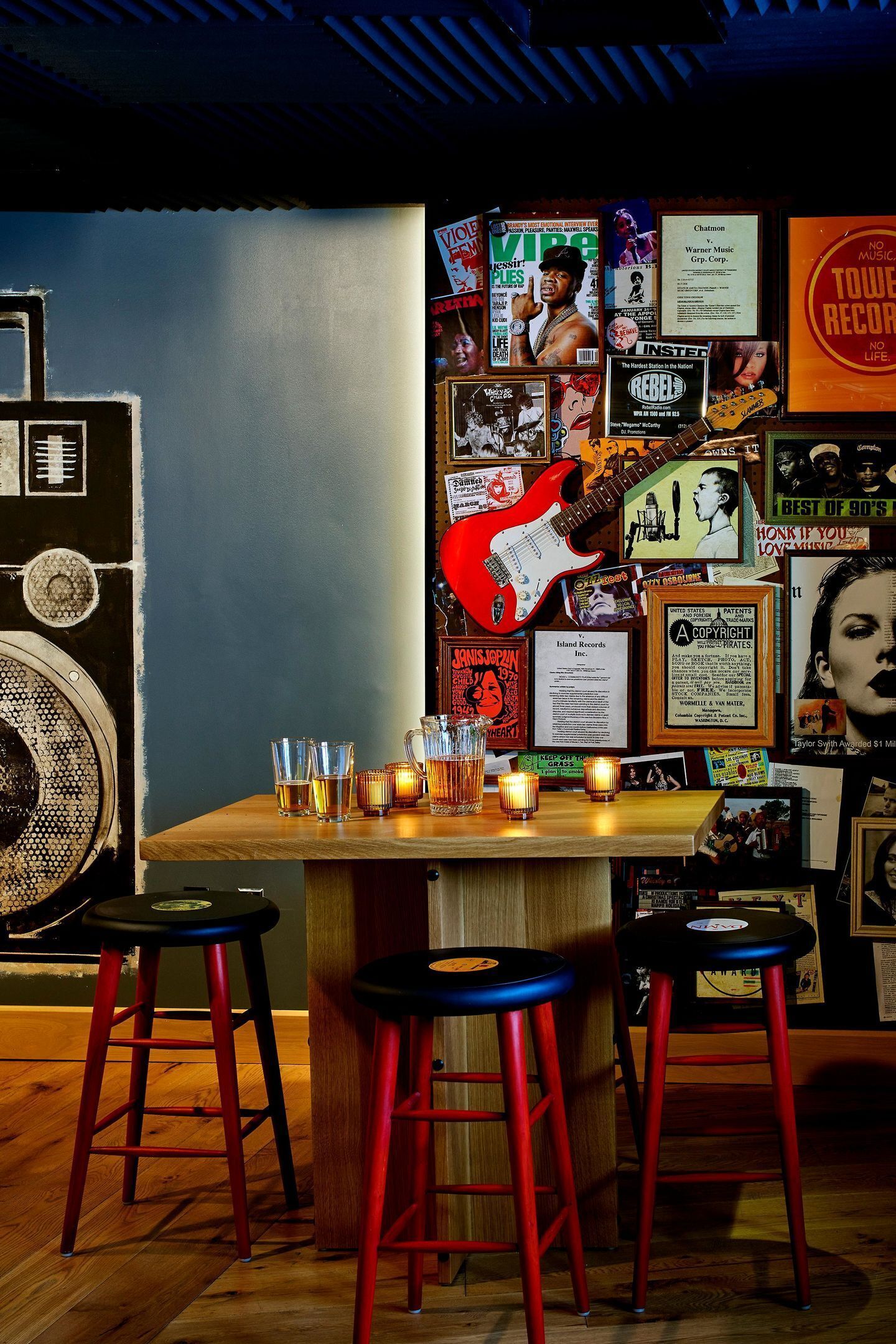 A bar area with stools, a guitar, and various posters on the wall.