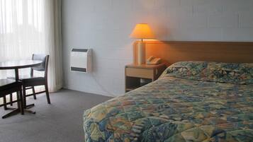 A hotel room with a bed, a bedside table with a lamp, a phone, and a wall-mounted air conditioner.