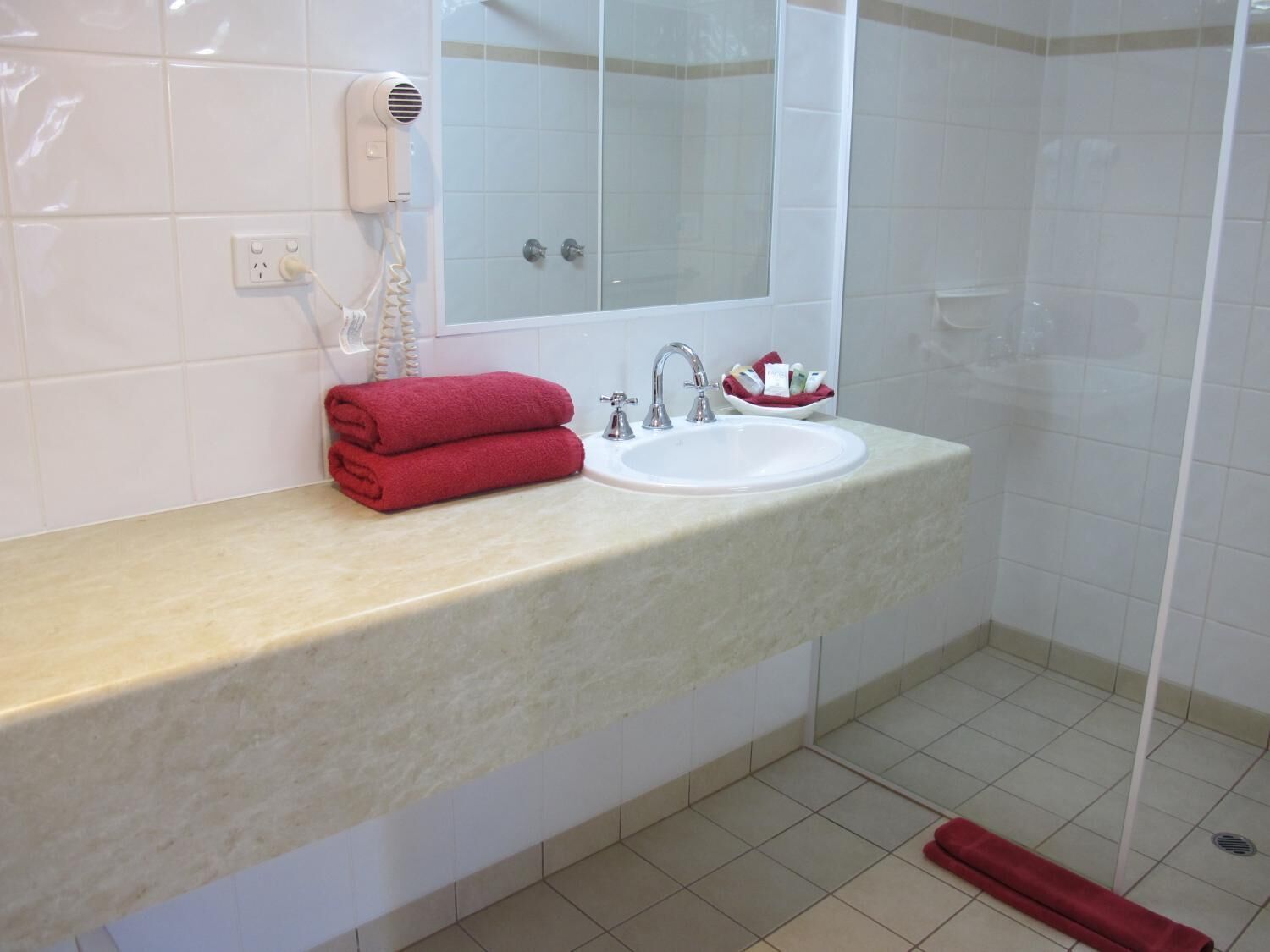 Casa de banho com lavatório, espelho e secador de cabelo na parede.