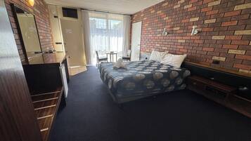 A hotel room with a bed, a desk, a chair, a small table, and a brick-patterned wall.