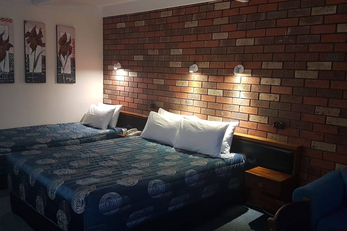 Una habitación con dos camas, una pared de ladrillo y tres lámparas fijadas a la pared.