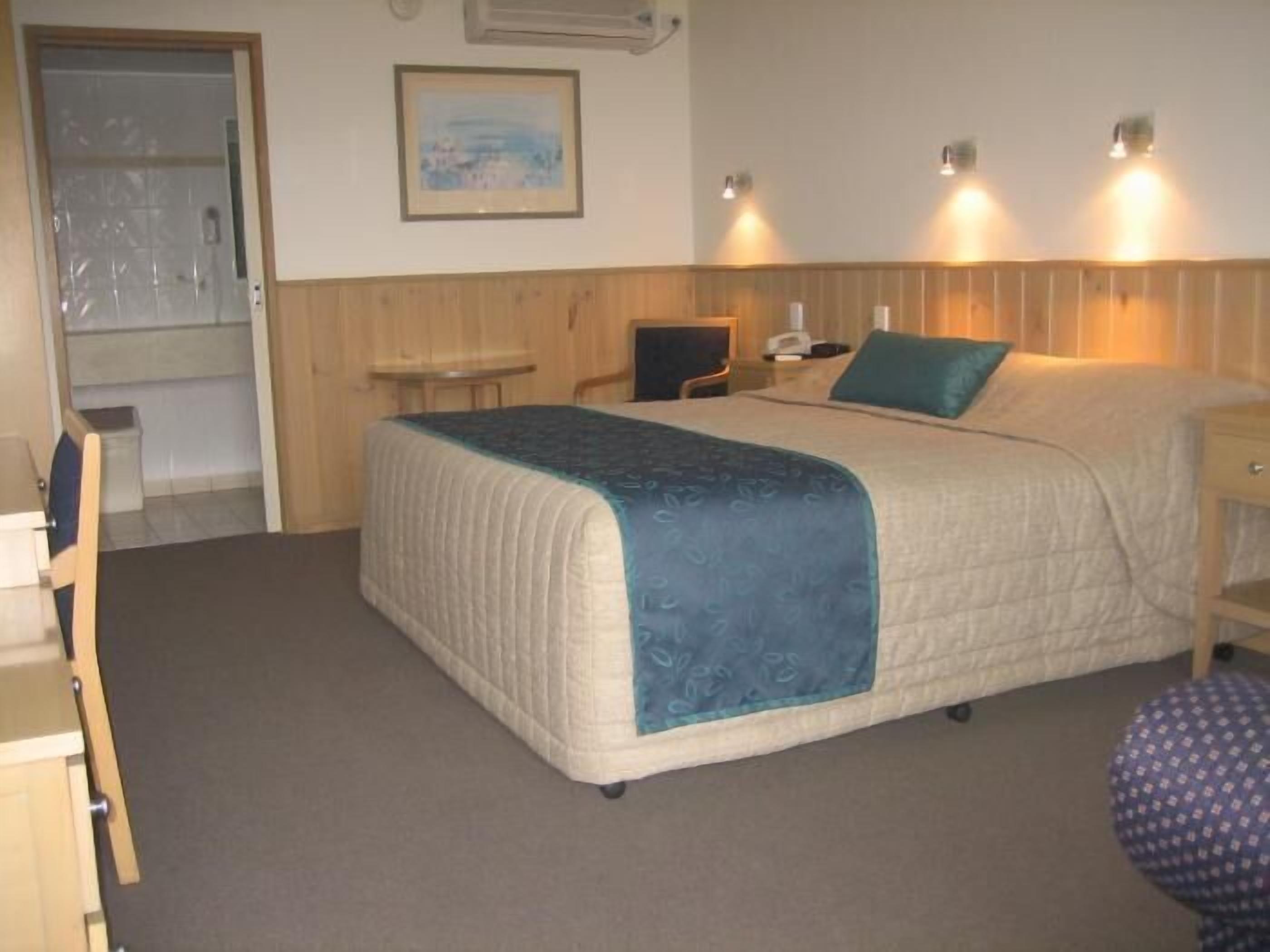 Una habitación de hotel con cama, escritorio, silla y una mesita.