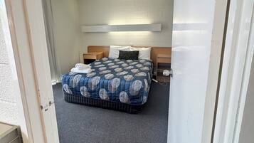 Una habitación pequeña con cama, mesitas de noche y estante en la pared.