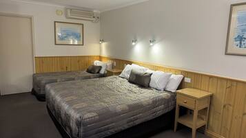 A hotel room with two beds, a wooden headboard, a nightstand, a framed picture on the wall, and an air conditioning unit.