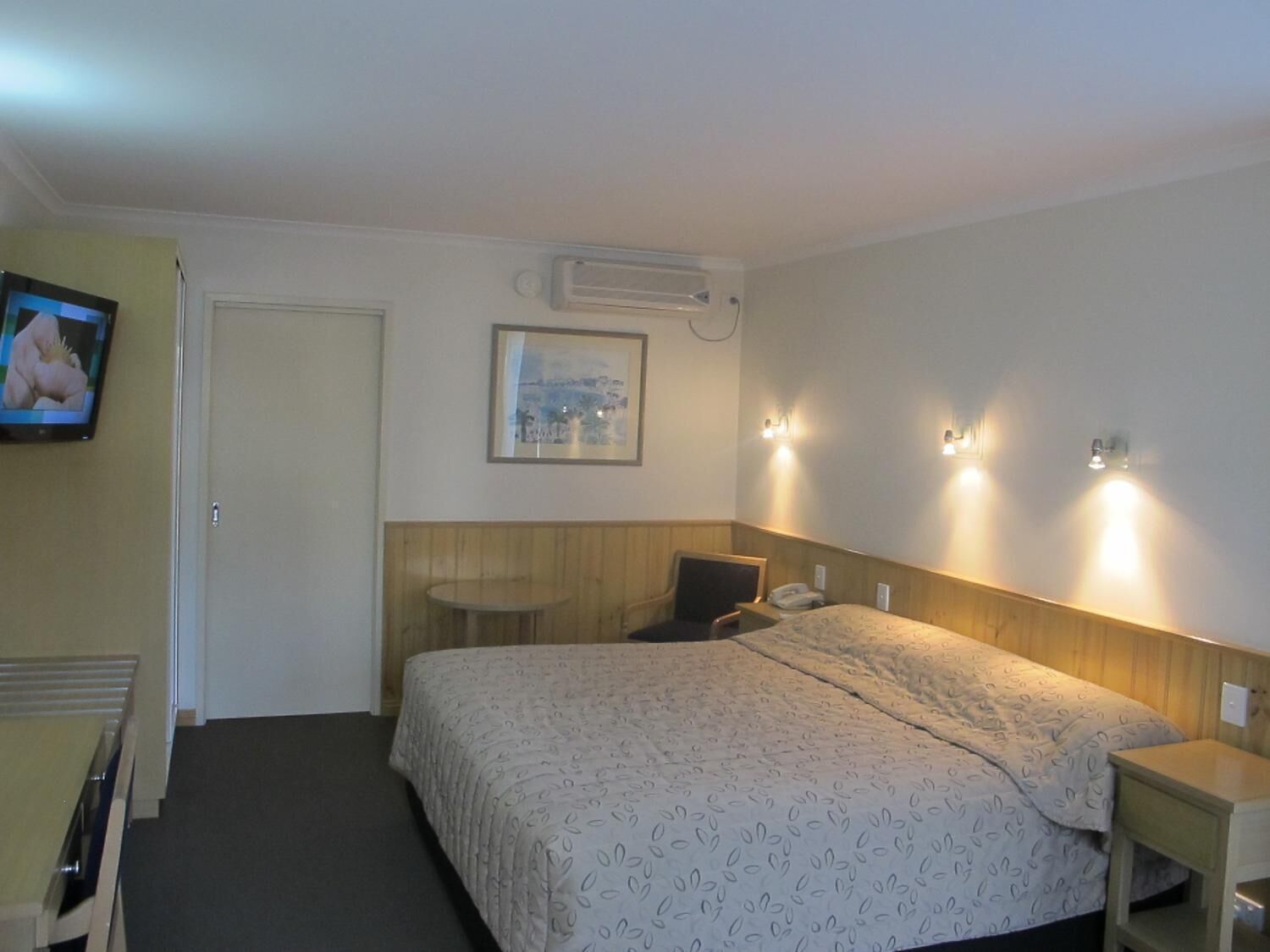 A hotel room with a bed, bedside table, chair, and a television on the wall.