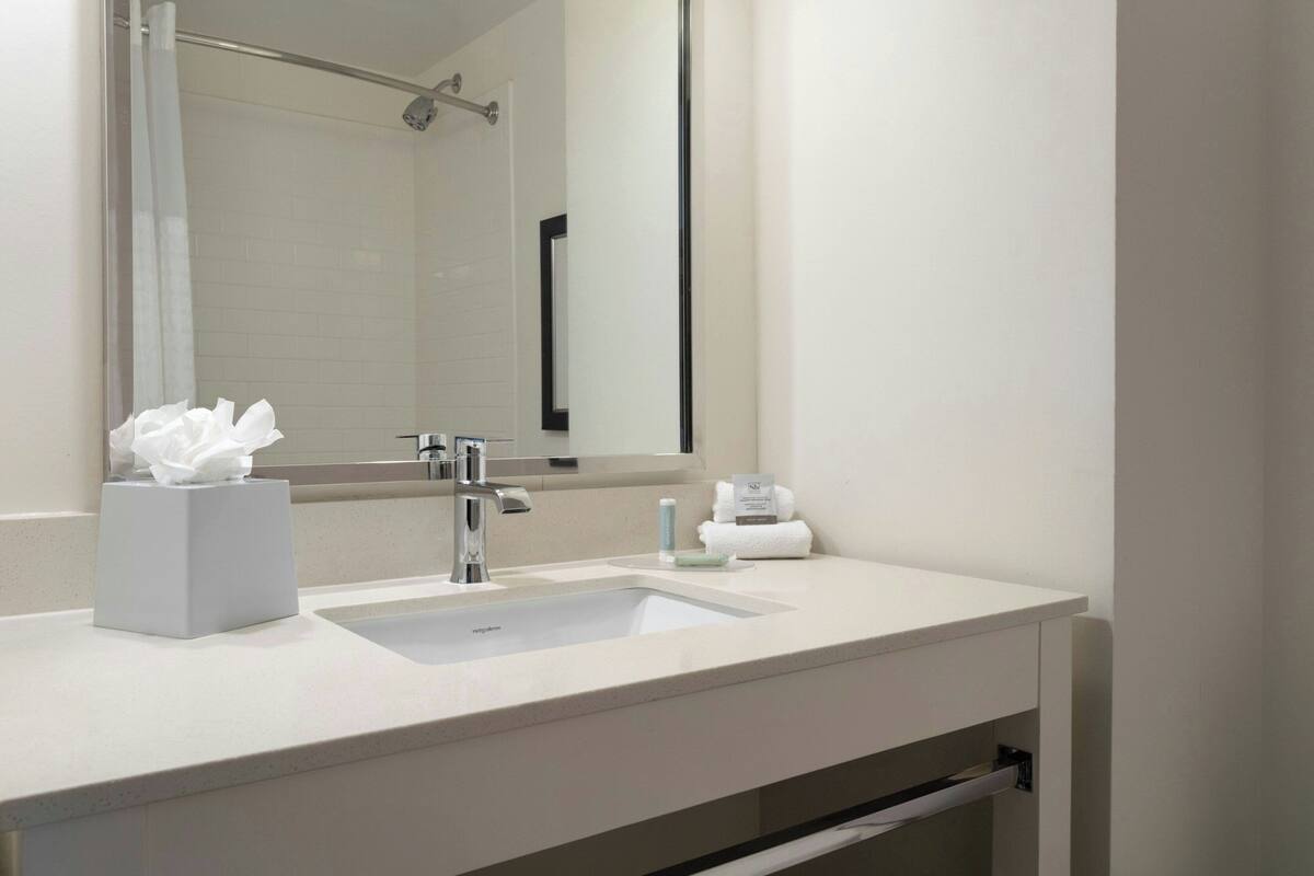 A modern bathroom with a white sink, a large mirror, and a towel rack.