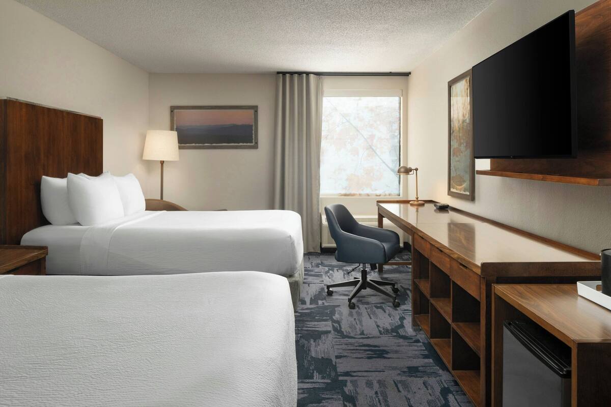 A hotel room with two beds, a desk, a chair, a TV, and a window with curtains.