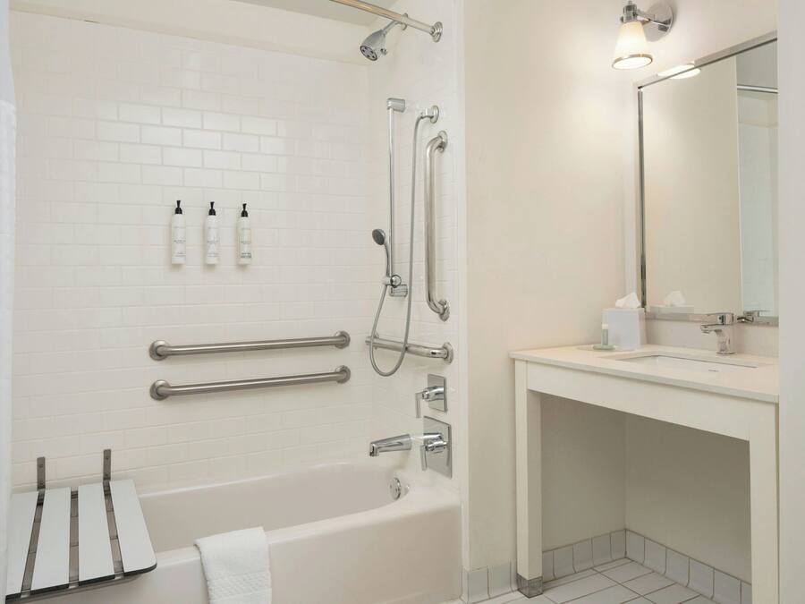 A modern bathroom with a white bathtub, a shower with grab bars, a vanity with a mirror, and toiletries on the wall.