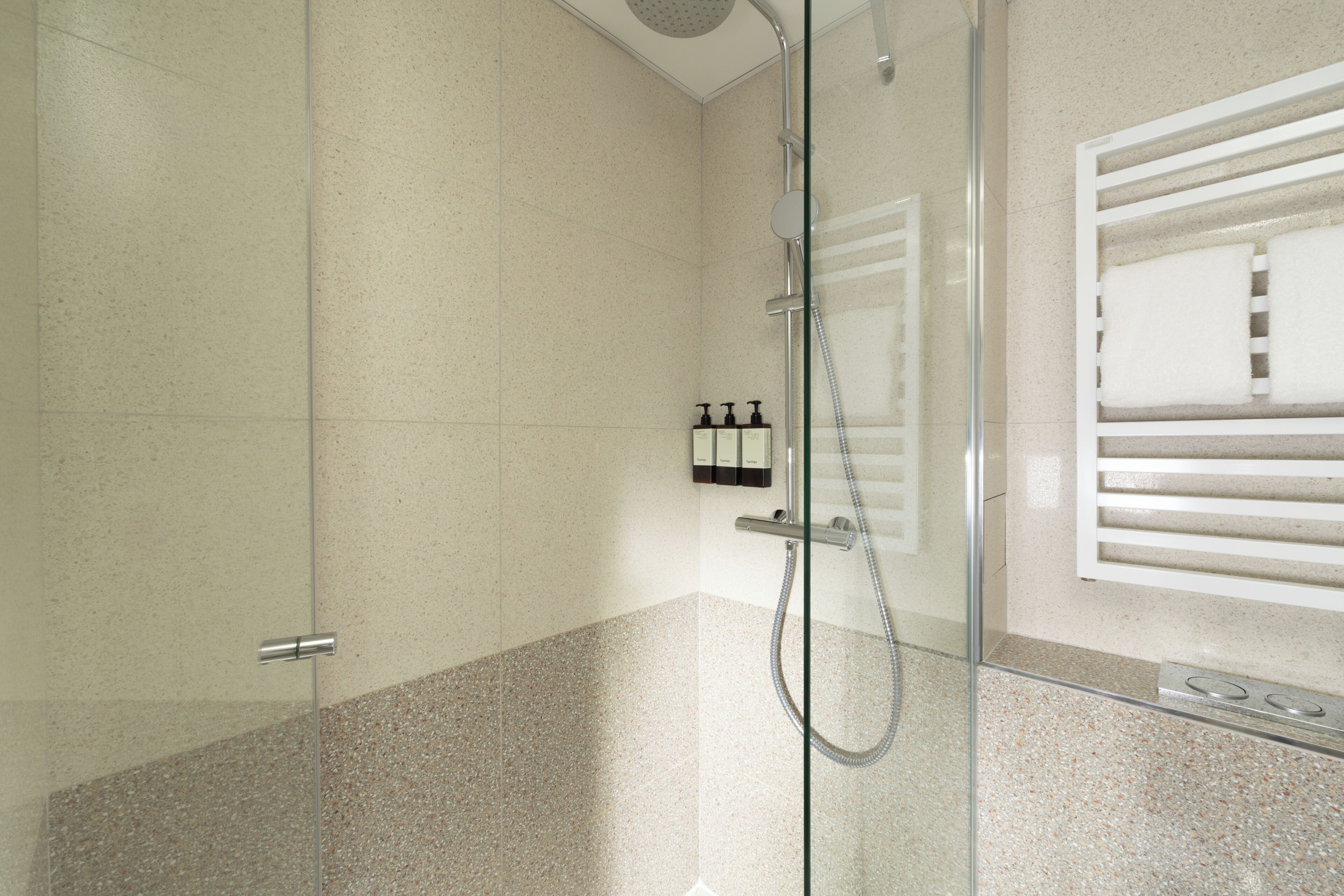 A modern bathroom with a glass shower enclosure, a towel rack, and a soap dispenser.