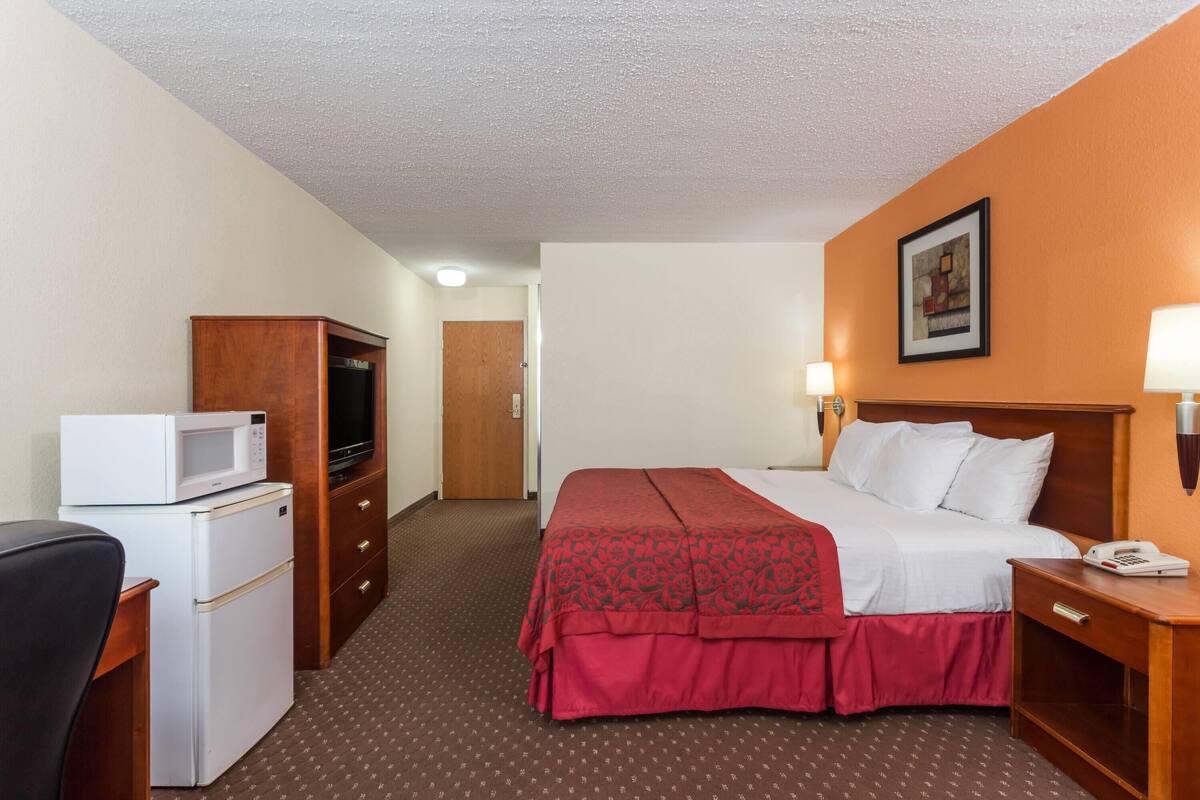Une chambre d’hôtel comprenant un lit, un bureau avec un micro-ondes, une commode et une porte donnant sur une autre pièce.