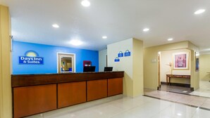 Taulell de recepció amb una paret blava i un cartell de Days Inn & Suites. Hi ha dos monitors d'ordinador a la taula, un petit aparell vermell i un quadre al mur.
