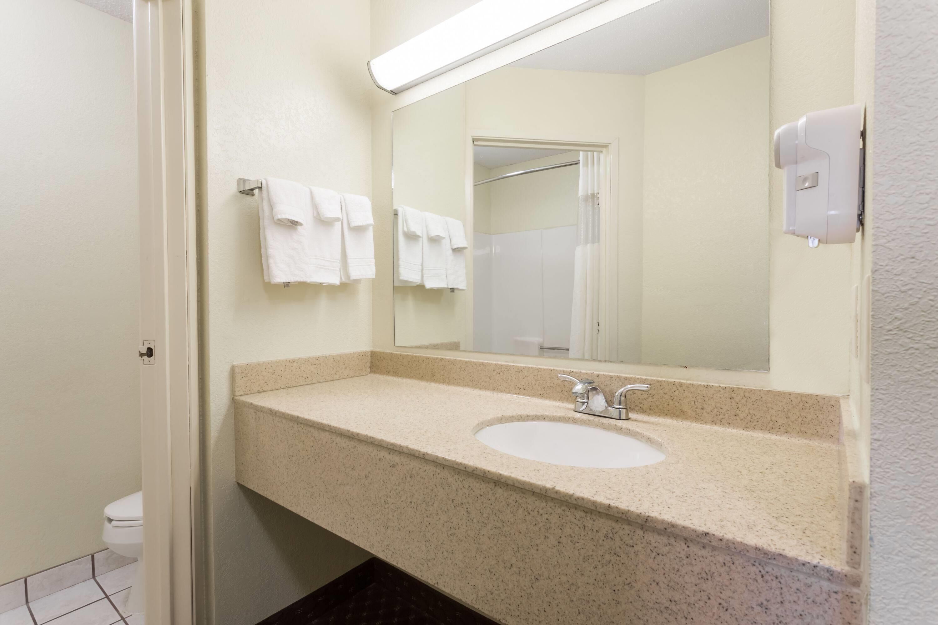 A bathroom with a beige countertop, a sink, a mirror, and a towel rack with white towels.