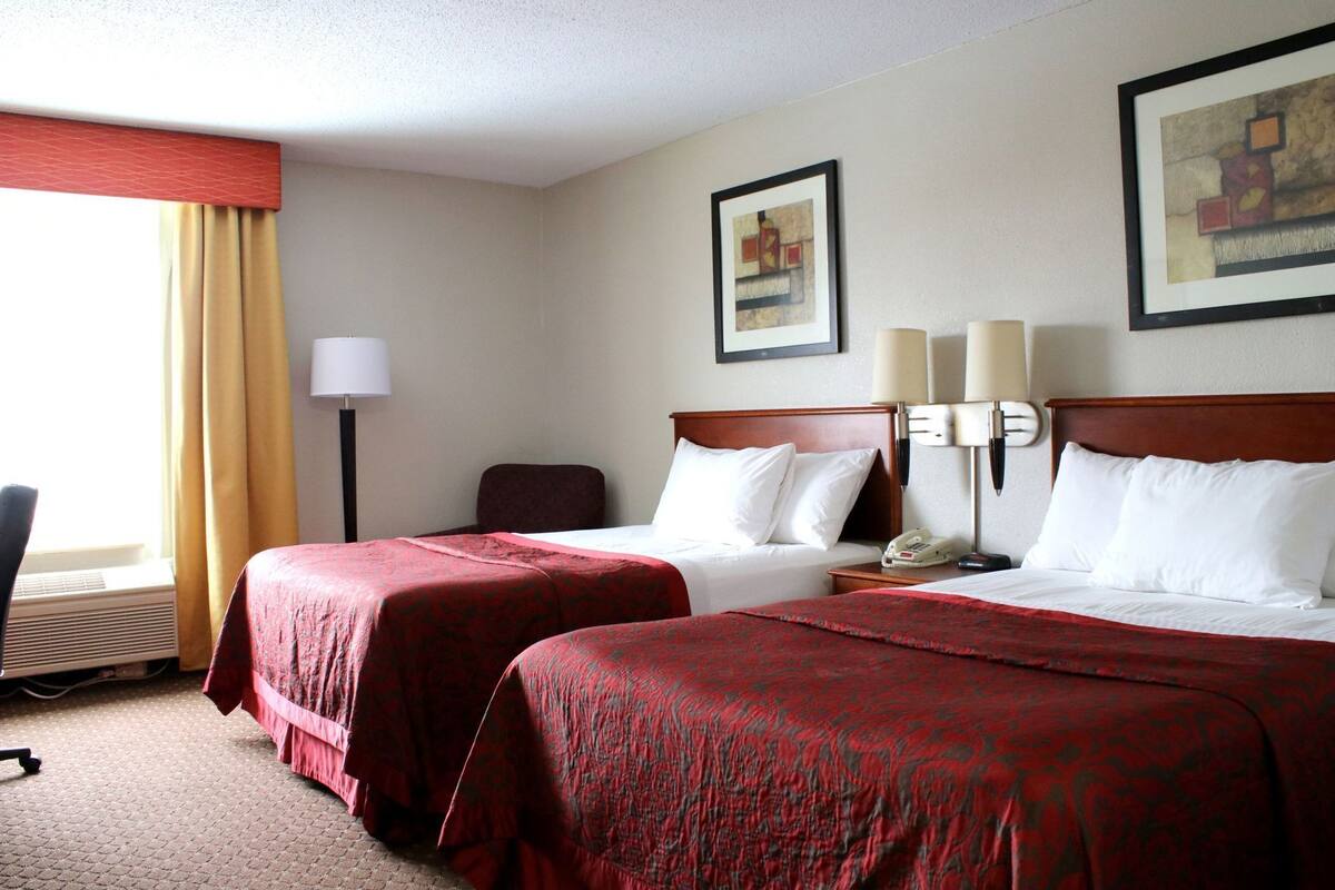 Une chambre d’hôtel avec deux lits, un bureau, une chaise, une lampe et des œuvres d’art accrochées aux murs.