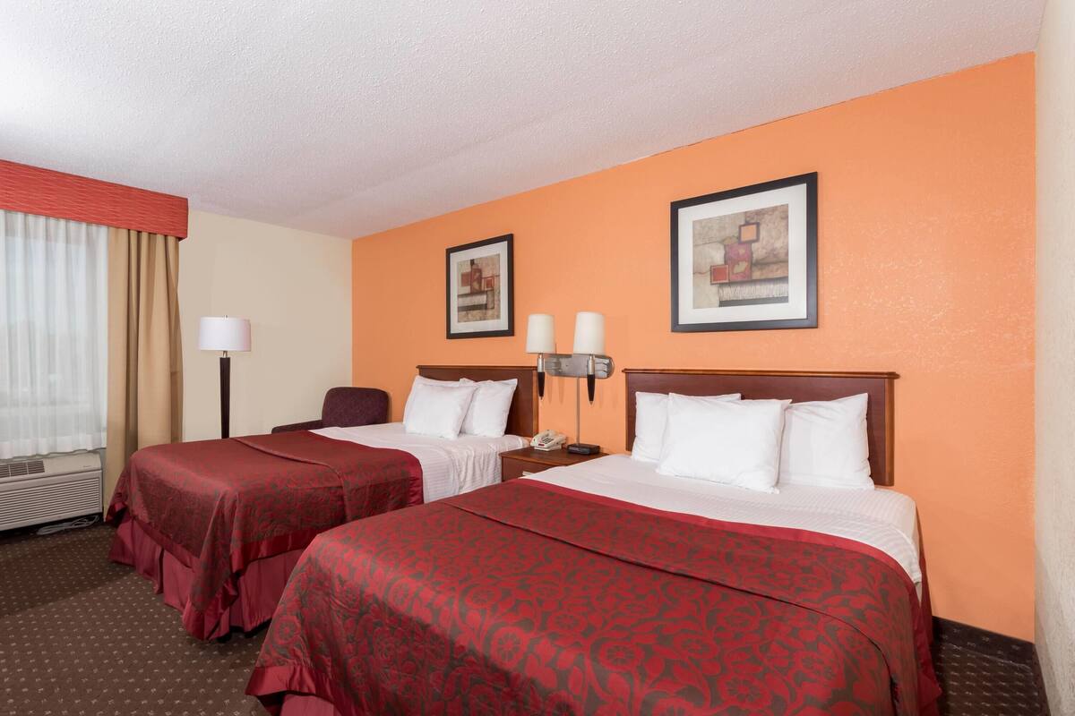 Une chambre d’hôtel avec deux lits, un bureau, une chaise, une lampe et des œuvres d’art encadrées accrochées au mur.