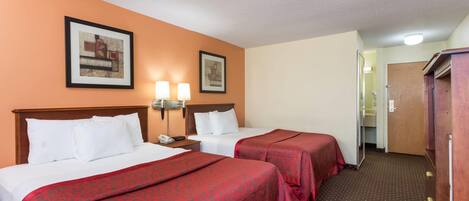A hotel room with two beds, a wooden headboard, a nightstand with a phone, two framed pictures on the wall, and a wooden wardrobe.