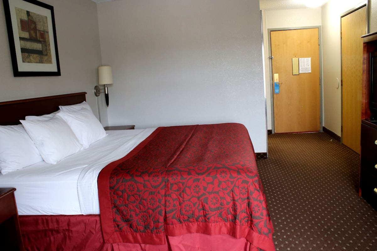 Une chambre d’hôtel avec un lit, une table de chevet, une lampe, une porte et un mur orné d’un tableau.