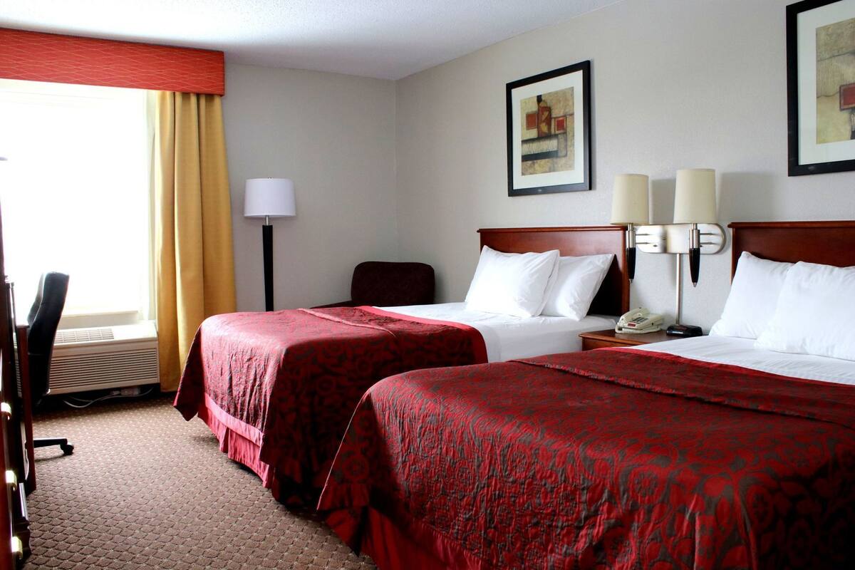 Une chambre d’hôtel avec deux lits, un bureau, une chaise, une lampe et un tableau au mur.