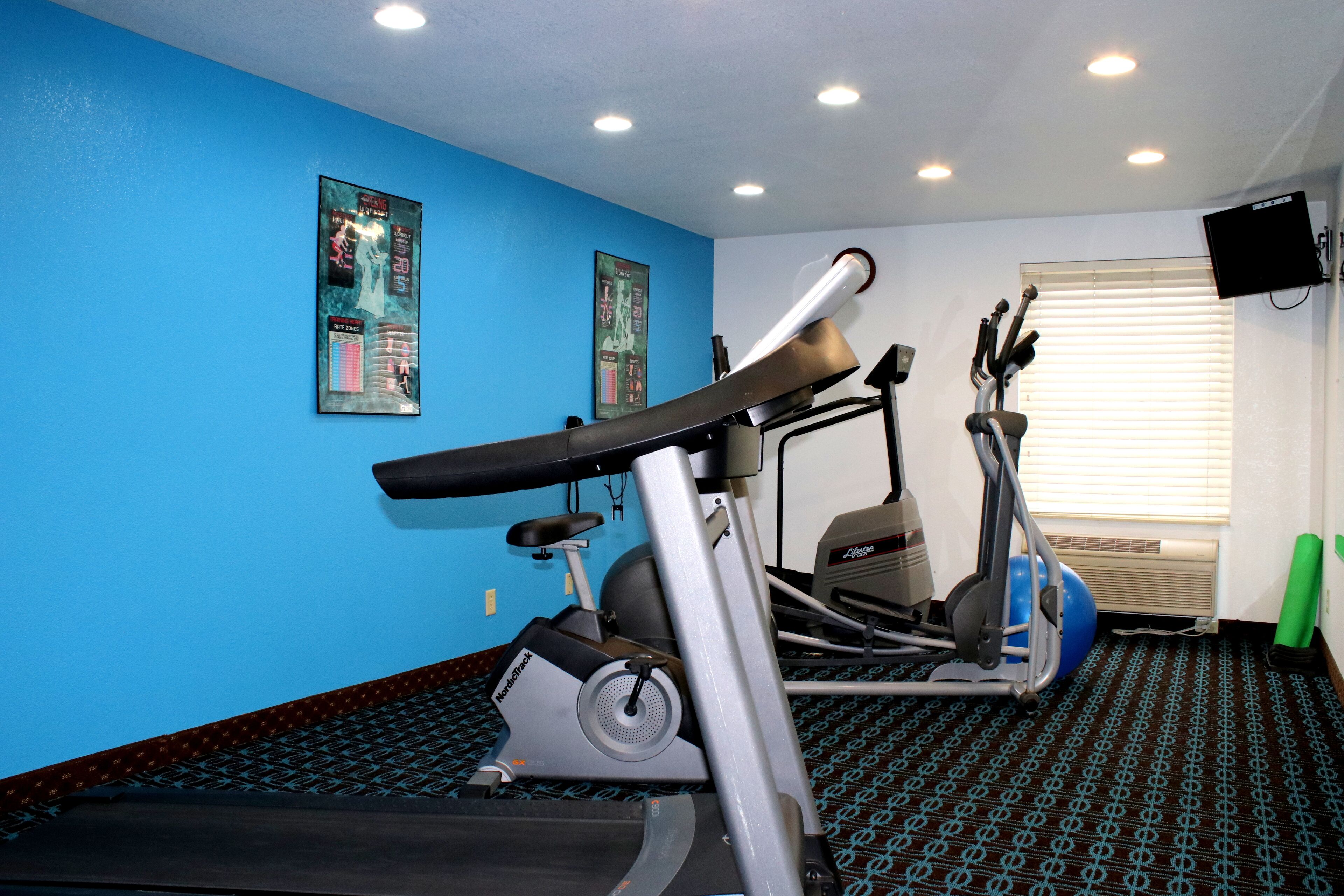 Un gimnasio con equipo de ejercicio, una pared azul y un televisor.