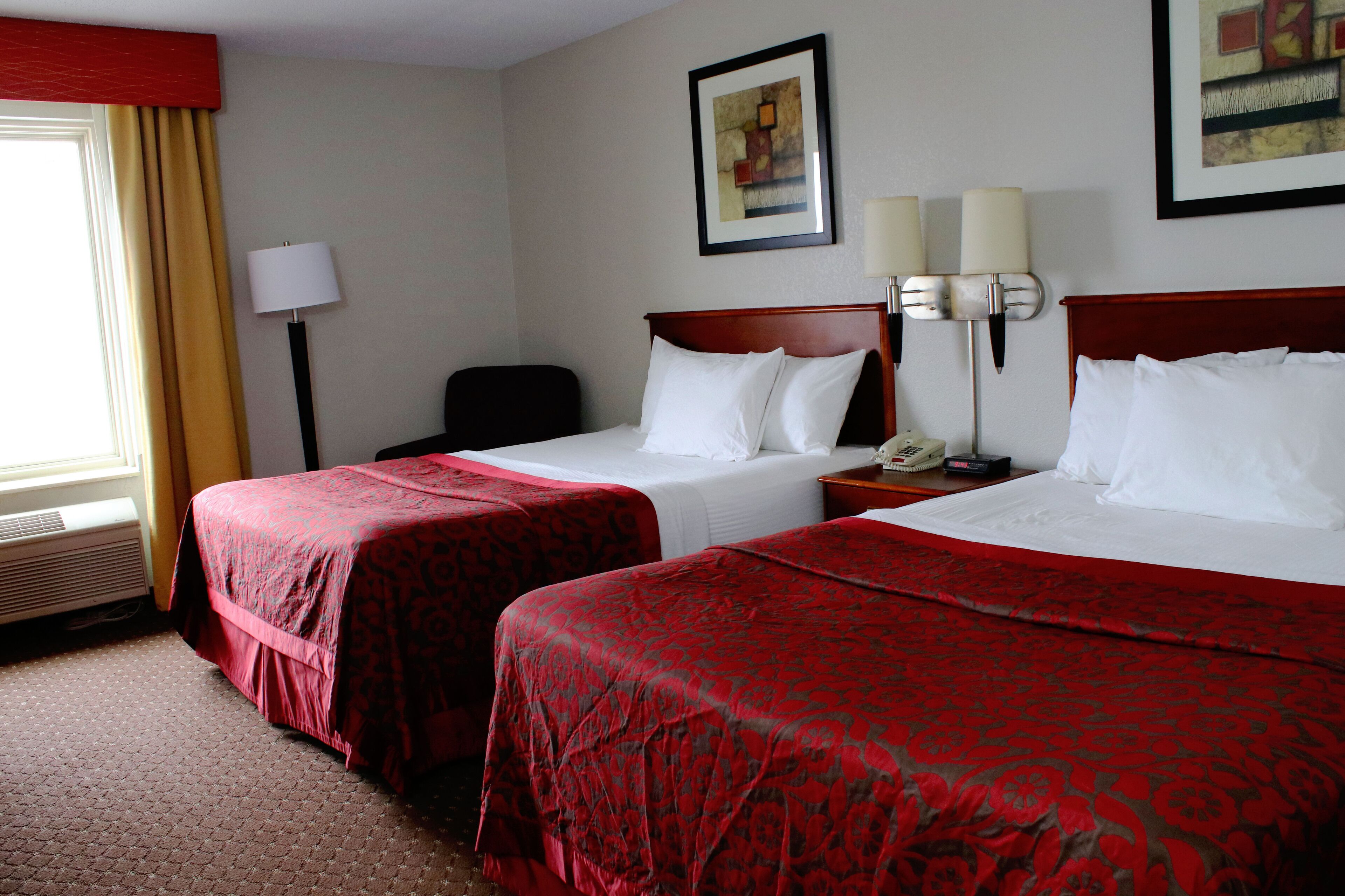 A hotel room with two beds, a desk, a chair, a lamp, and a painting on the wall.