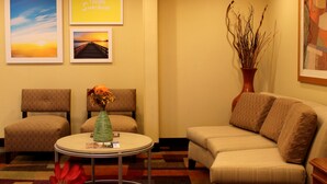 Rebedor d'hotel amb una taula rodona, dues butaques, un sofà i obra d'art mural que inclou un tramunt i un cartell amb la frase 'Hello Sunshine'.