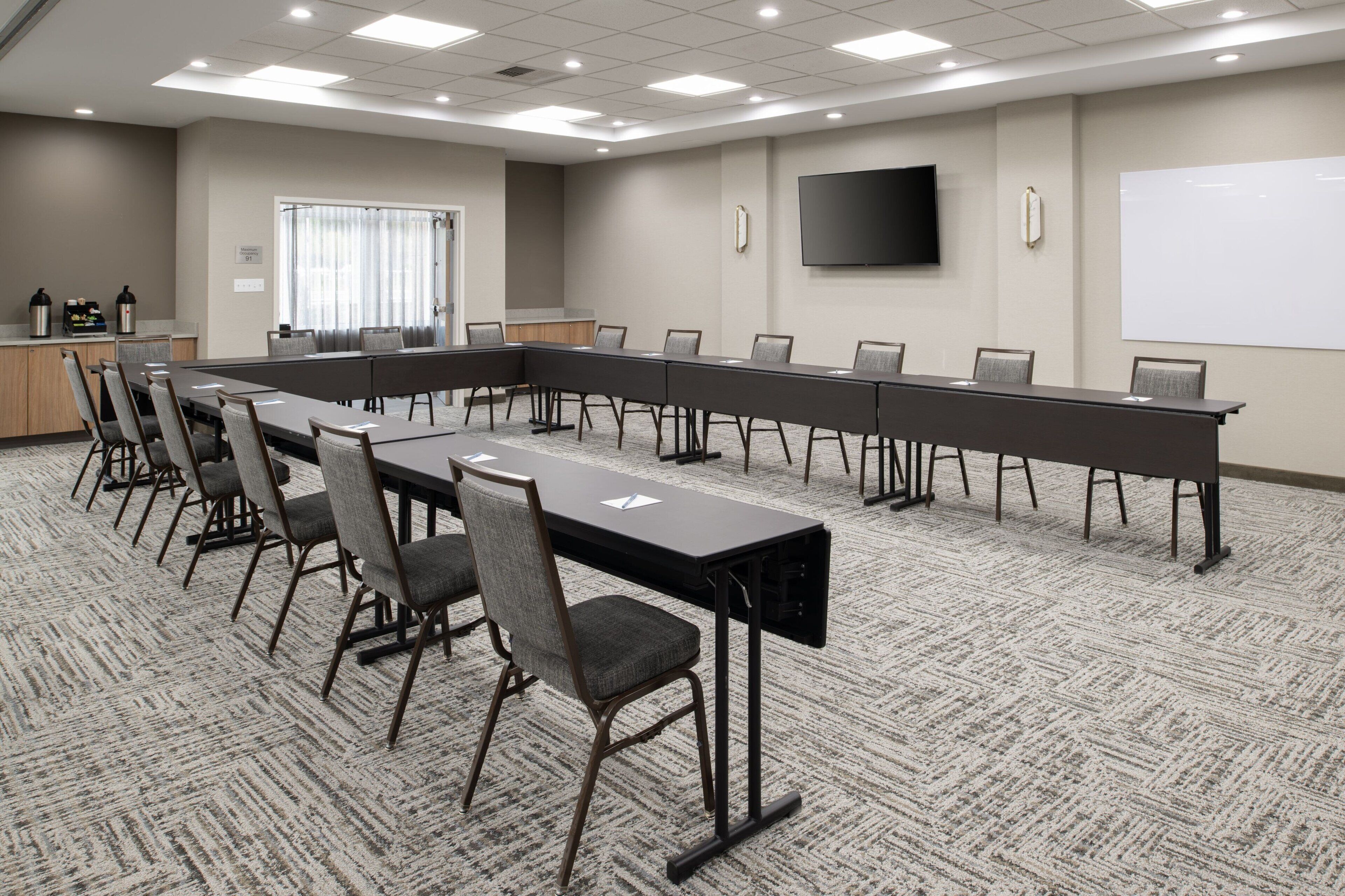 A conference room with a long table, chairs, a whiteboard, and a TV on the wall.