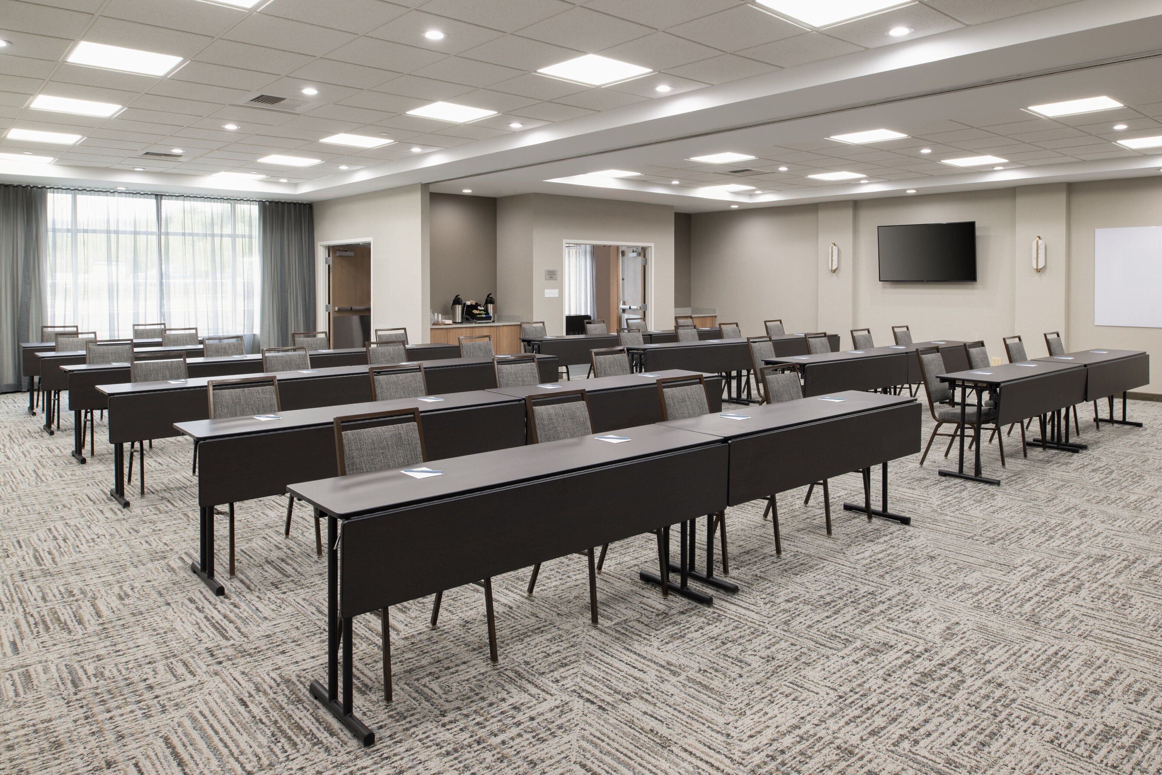 A conference room with multiple tables and chairs, a large screen, and a projector.