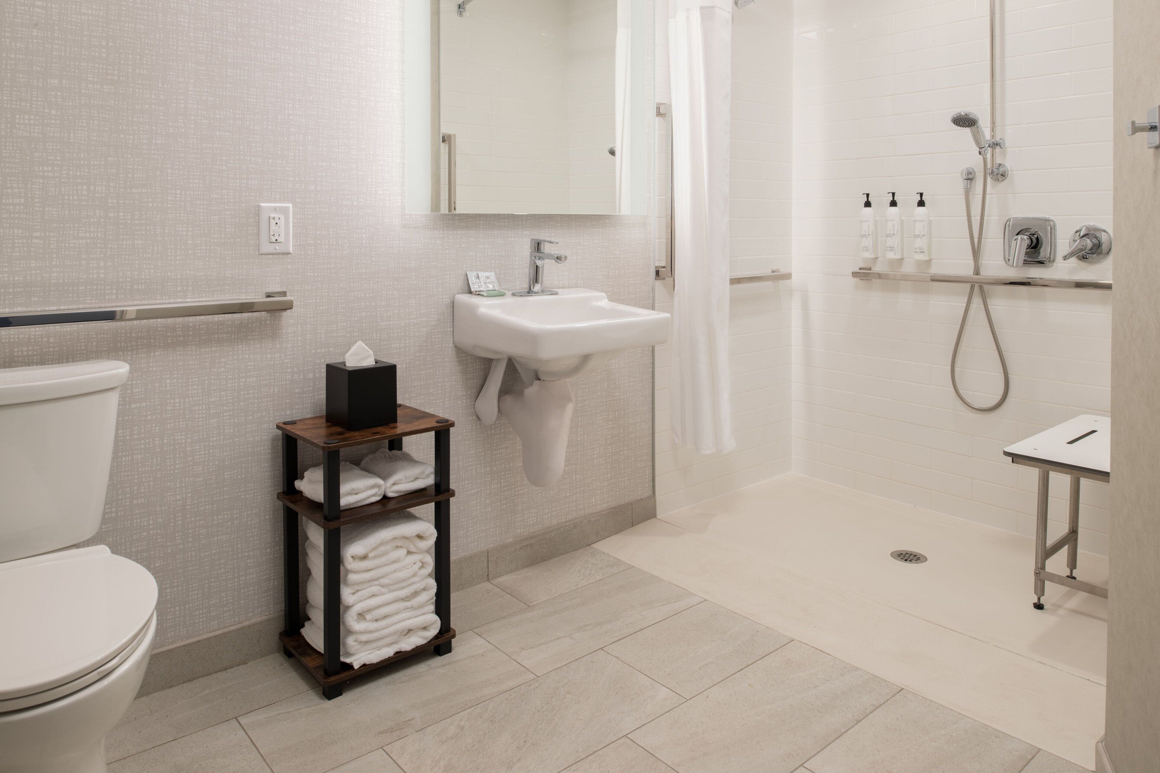 A modern bathroom with a toilet, sink, and shower. There is a towel rack and a shelf with toiletries.