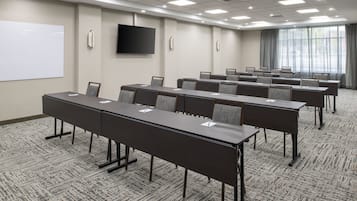 Ein Konferenzraum mit langem Tisch, Stühlen, einer Whiteboard-Tafel und einem Fernsehbildschirm.