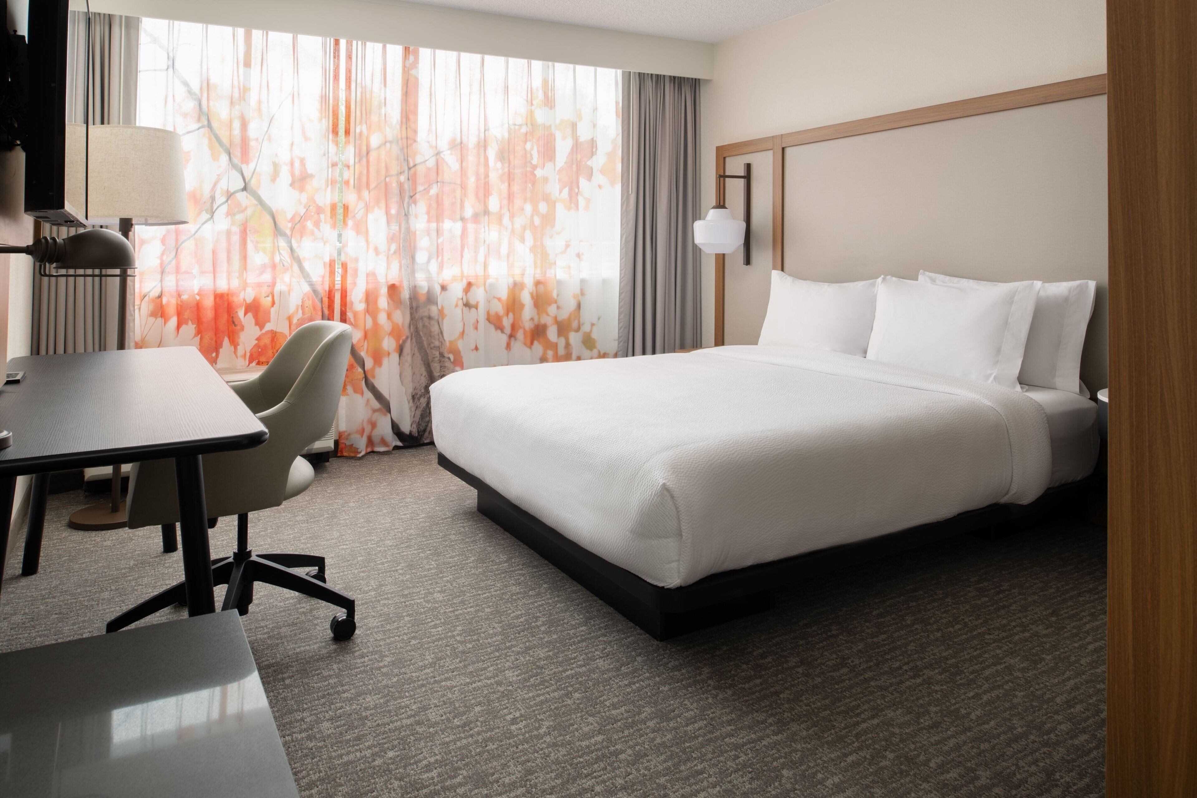 A hotel room with a large bed, a desk, a chair, and a lamp.