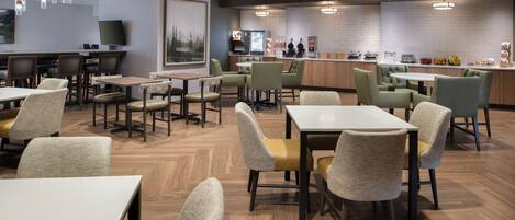A modern restaurant with multiple dining tables and chairs, a bar area, and a kitchen in the background.