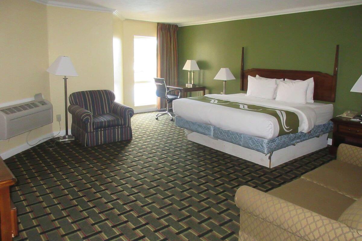 A hotel room with a bed, a chair, a desk, and a lamp.