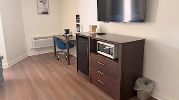 A compact room with a desk, chair, kitchenette, and a mounted TV.