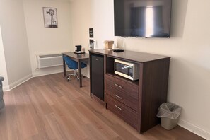 A compact room with a desk, chair, kitchenette, and a mounted TV.