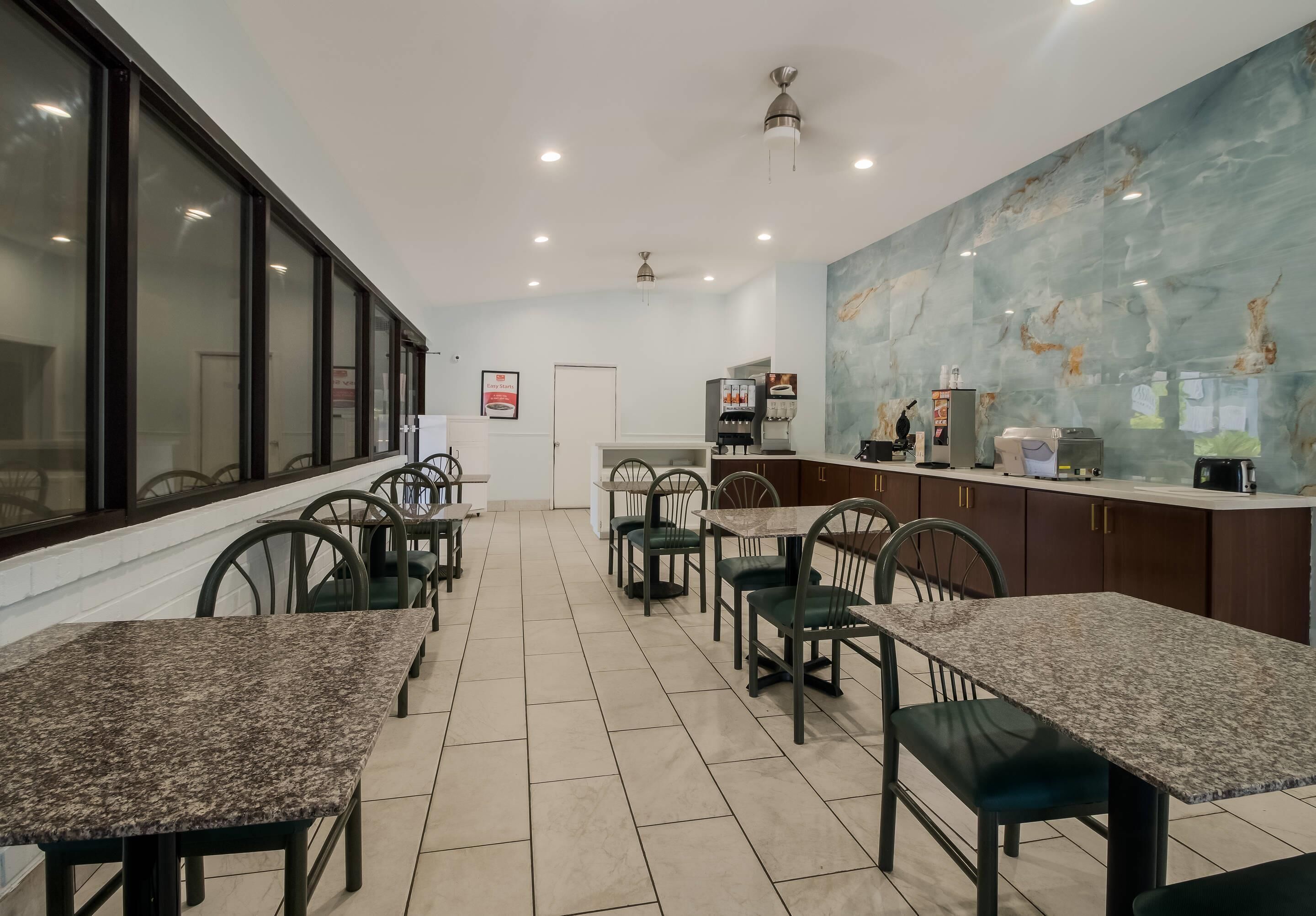 Un restaurante con varias mesas y sillas, una zona de cocina y un mural grande en la pared.