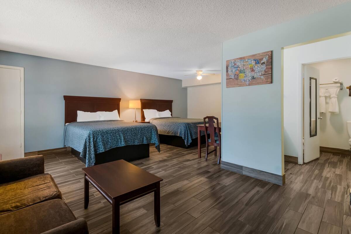 A room with two beds, a wooden table, a chair, and a bathroom door.