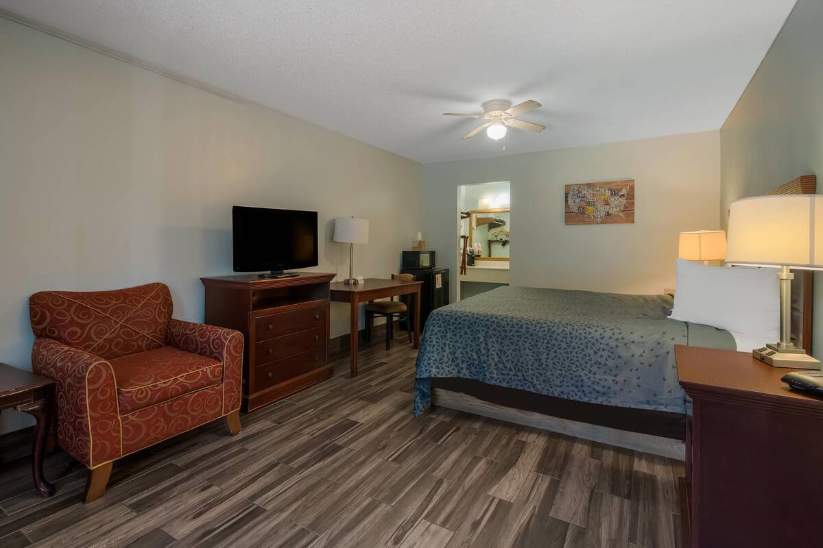 A hotel room with a bed, a desk, a chair, a television, and a ceiling fan.