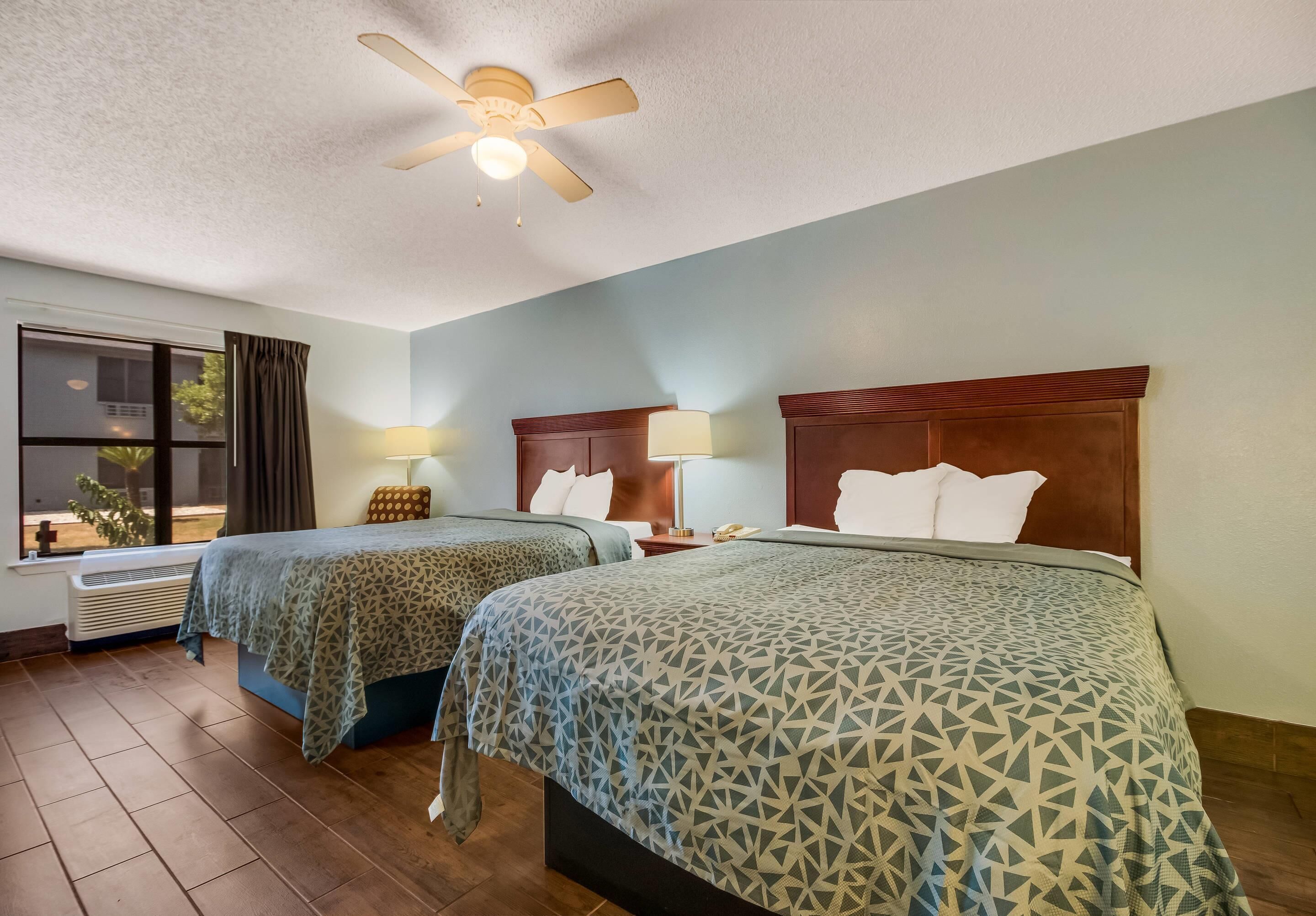 Une chambre d’hôtel avec deux lits, un ventilateur de plafond, une fenêtre avec des rideaux et une table de chevet avec une lampe.