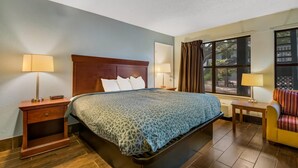 A hotel room with a large bed, two bedside tables with lamps, a window with curtains, and a small table with a chair.