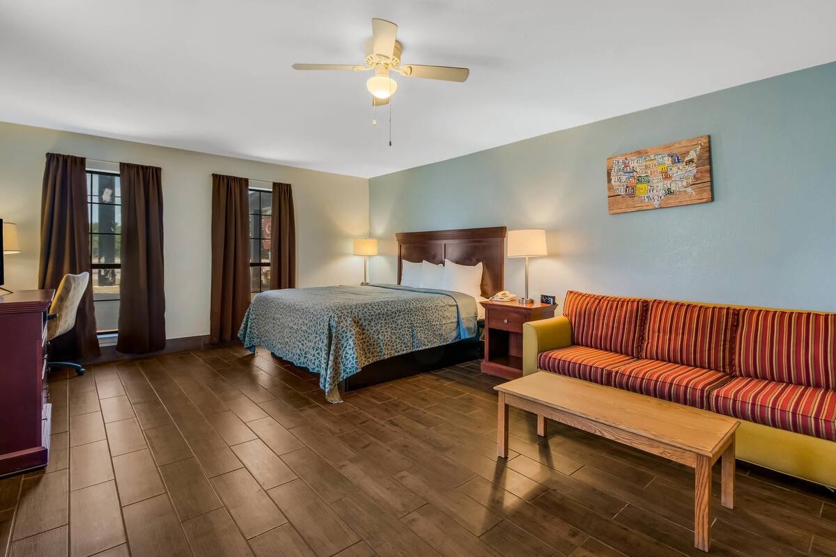 A hotel room with a bed, a sofa, a desk, and a ceiling fan.