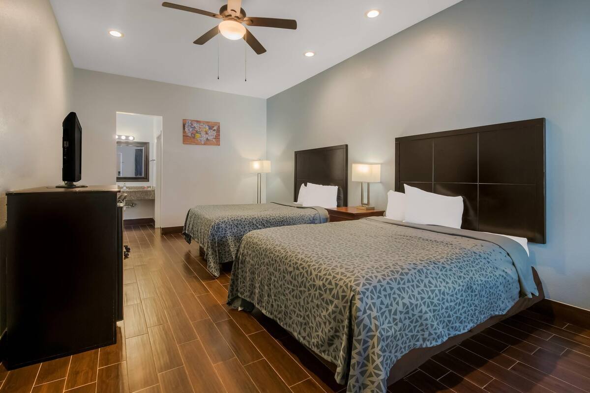 A hotel room with two beds, a ceiling fan, a desk, and a mirror.