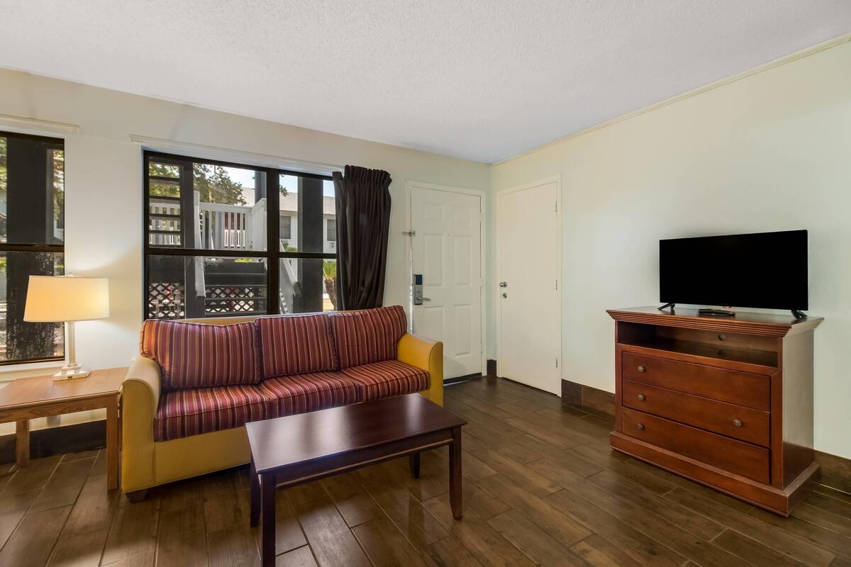A living room with a sofa, a coffee table, a TV on a wooden cabinet, and a window with curtains.