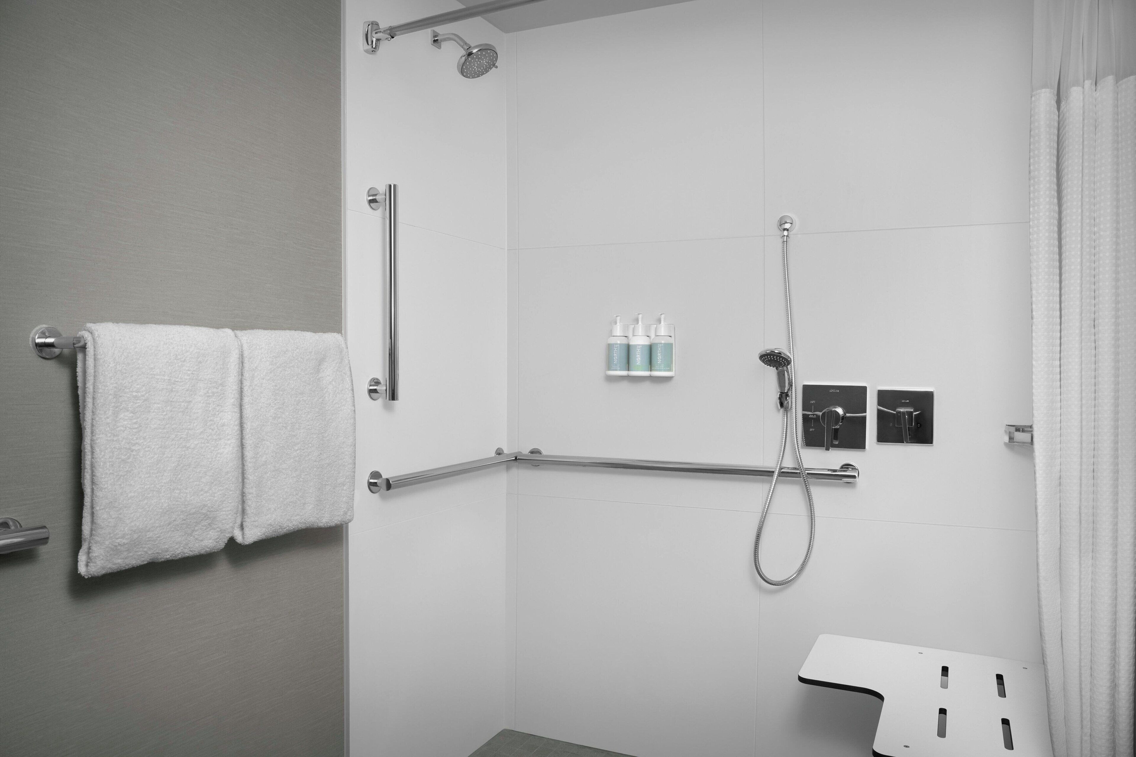 A modern shower area with a grab bar, a towel rack, and a showerhead.