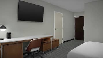 A hotel room with a desk, chair, bed, and a large flat-screen TV.